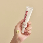 Une main tient un tube blanc de KSECRET Crème Contour Yeux SEOUL 1988 Liposome Rétinien 4% + Haricot Fermenté 30ml sur un fond beige neutre, en appliquant une noisette sur le dos de la main. Dakar