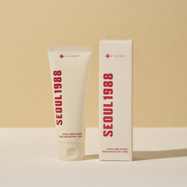 Un tube et une boîte de KSECRET SEOUL 1988 Séoul 1988 Crème Hydratante Snail Mucin 93% + Rice, avec un texte rouge en gras, se détachent sur un fond beige clair. Le tube est légèrement en avant de la boîte, projetant une ombre douce. Dakar