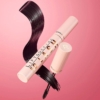 Un tube rose ouvert de mascara 5D Lash Mascara Lift and Define de 14 ml de MakeUp Revolution, ressemblant au look Lash Sensational Sky, révèle la brosse. Des volutes de mascara artistiques ornent le fond, tandis que le mot « Revolution » apparaît avec audace sur le tube sur un fond rose. Dakar