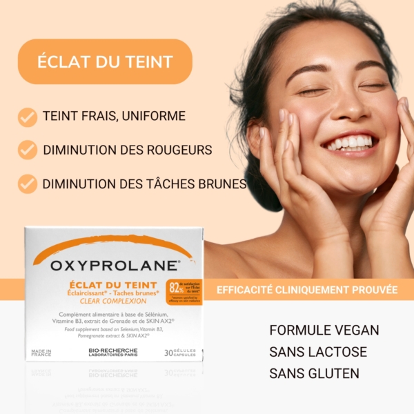 Une femme sourit les yeux fermés et se touche le visage, mettant en avant les bienfaits d'Oxyprolane Éclat du Teint Anti Taches Éclaircissant : un teint frais et uniforme avec des rougeurs et des taches brunes atténuées. Ce produit vegan est également sans lactose et sans gluten. Dakar