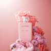 Un flacon de parfum rose étiqueté « La Rive Poétique » est entouré d'un arrangement de roses roses et de pivoines douces. Le fond est d'un rose assorti, créant une esthétique florale harmonieuse et élégante. Dakar