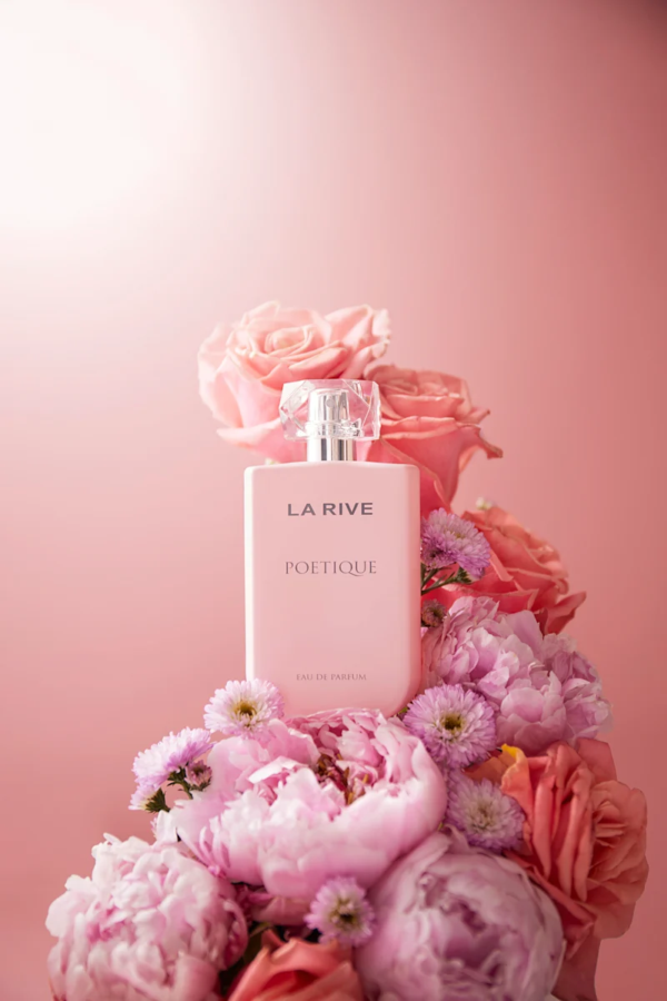 Un flacon de parfum rose étiqueté « La Rive Poétique » est entouré d'un arrangement de roses roses et de pivoines douces. Le fond est d'un rose assorti, créant une esthétique florale harmonieuse et élégante. Dakar