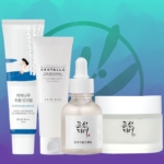 Sur un fond bleu et bleu sarcelle, quatre produits de routine de soins de la peau ANTI IMPERFECTIONS sont présentés : un tube de crème solaire, une mousse nettoyante, un flacon compte-gouttes et un pot, avec du texte coréen et anglais sur les étiquettes. Dakar