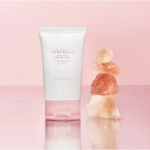Un tube de Skin1004 Gel Crème Léger Anti Pores Dilatés Centella de Madagascar 75 ml repose élégamment sur une surface rose réfléchissante, contrastée par des cristaux de sel de l'Himalaya empilés qui renforcent l'attrait minimisant les pores de la crème. Dakar