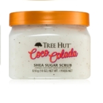 Pot de gommage au sucre de karité à la pastèque Tree Hut 510 g (Copie) avec un couvercle orange. L'étiquette indique le nom du produit et le poids net de 510 g (18 oz). Il a une texture lisse et crémeuse avec des taches visibles, offrant une essence revigorante similaire au Coco Colada. Dakar