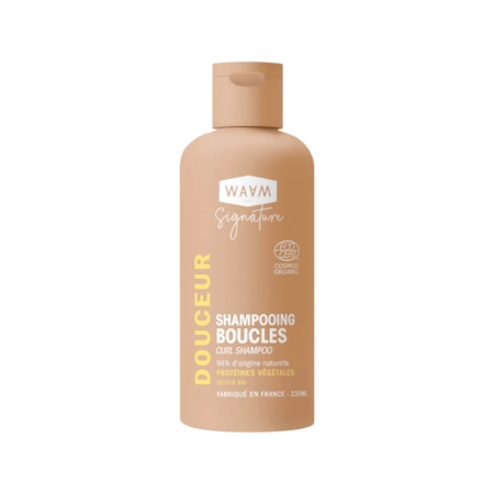 Un flacon beige de Waam Shampooing Boucles BIO 230ml avec un texte blanc et jaune se tient debout sur un fond blanc. L'étiquette met en évidence les ingrédients d'origine naturelle et la teneur en protéines. Dakar