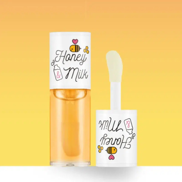 Tube de gloss à lèvres étiqueté « Honey & Milk » avec des illustrations d'abeilles et de bouteilles de lait sur un fond jaune dégradé. Le gloss est partiellement ouvert, laissant apparaître l'applicateur. Dakar