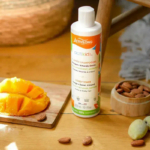 Un flacon d'après-shampoing Actikids est exposé sur une surface en bois. À proximité, des morceaux de mangue et un petit bol rempli d'amandes entières. L'éclairage chaleureux du décor évoque une ambiance naturelle et fraîche. Dakar