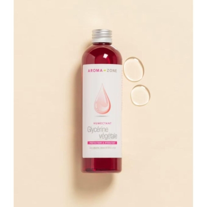 Un flacon transparent d'émollient glycérine végétale Aroma Zone de 250 ml contenant un liquide rouge est posé sur un fond beige. Deux gouttes rondes sont disposées à côté, et l'étiquette affiche un motif de gouttelettes roses. Dakar