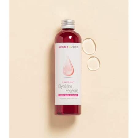 Un flacon transparent d'émollient glycérine végétale Aroma Zone de 250 ml contenant un liquide rouge est posé sur un fond beige. Deux gouttes rondes sont disposées à côté, et l'étiquette affiche un motif de gouttelettes roses. Dakar