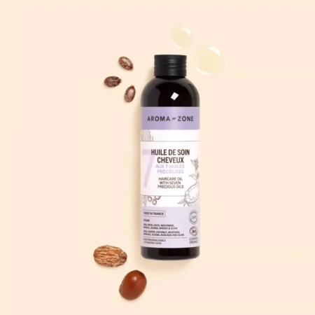 Une bouteille d'Aroma Zone Huile de soin Cheveux 250 ml repose sur un fond beige, étiquetée « Huile de soin cheveux aux 7 huiles précieuses », avec des noix et des graines à proximité suggérant des ingrédients naturels. Idéal à utiliser avec le Masque capillaire Aroma Zone Base pour une meilleure nutrition des cheveux. Dakar
