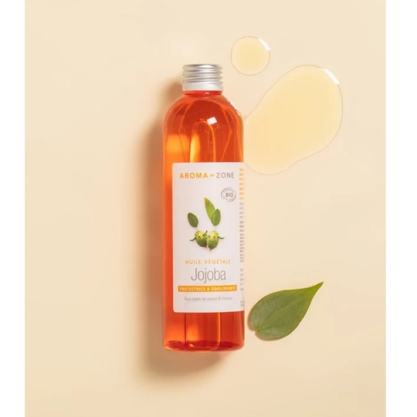 Un flacon d'Huile de Jojoba BIO Aroma Zone 100 ml repose sur une surface couleur crème. D'un orange vif et doté d'un bouchon argenté, ce flacon arbore une étiquette verte à l'effigie d'une plante. À proximité, une feuille verte luxuriante et une touche d'huile essentielle envoûtante évoquent l'essence de l'Huile de Coco Aroma Zone. Dakar