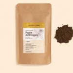 Un paquet brun de 250 g étiqueté "Aroma Zone Poudre de Bhringaraj" avec des motifs botaniques repose à côté d'un tas de poudre brun foncé sur une surface beige clair. Dakar