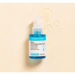 Un flacon pompe bleu de 30 ml d'Aroma Zone Sérum concentré d'Acide hyaluronique 3,5 % est posé sur un fond beige clair, à côté de gouttes de sérum. L'étiquette met en avant ses propriétés hydratantes et anti-âge, idéalement associées à l'Aroma Zone Sérum concentré Vitamine C pour une peau éclatante. Dakar