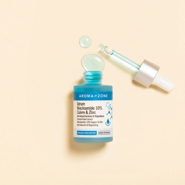 L'Aroma Zone Sérum concentré Niacinamide 10%, Cuivre et Zinc 30 ml repose sur une surface beige, faisant écho à l'Aroma Zone Elixir de fleurs précieuses de Rose. Son flacon et son compte-gouttes turquoise suggèrent une symphonie florale dans chaque goutte. Dakar