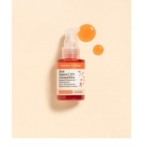 Sur un fond beige se trouve un flacon d'Aroma Zone Sérum concentré Vitamine C 10 % et Astaxanthine 30 ml. La pompe transparente présente un liquide orange, avec deux gouttes à proximité. L'étiquette met en avant les ingrédients et les bienfaits vegan du sérum. Dakar