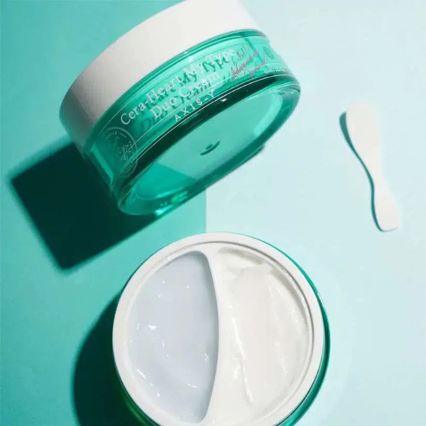 Un pot ouvert de crème de soin à double texture, mi-blanche, mi-translucide, sur une surface bleu sarcelle clair. Une petite spatule est posée à côté du pot. Le pot est étiqueté « Cera-Heart My Type Duo Cream ». Dakar