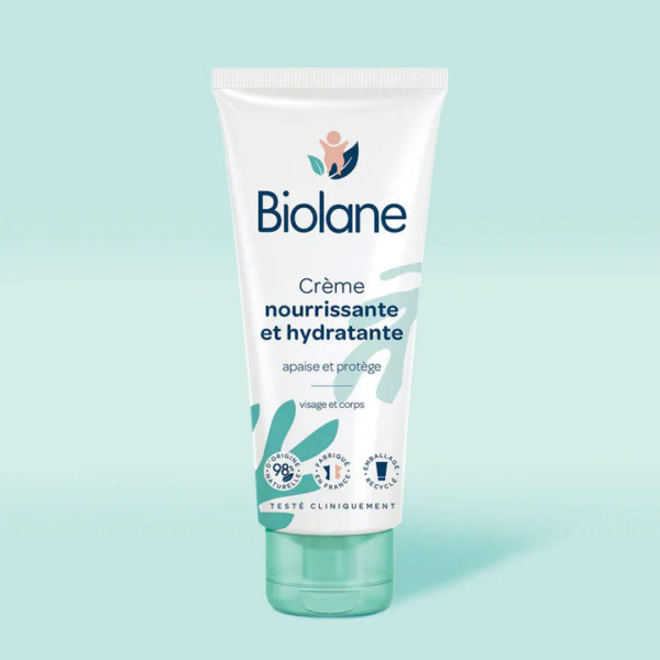 Un tube de crème hydratante Biolane est présenté sur un fond bleu sarcelle clair. L'étiquette met en avant ses propriétés nourrissantes et hydratantes, avec des pictogrammes indiquant 98 % d'origine naturelle et des tests dermatologiques. Dakar