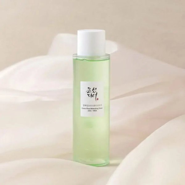 Une fine bouteille verte translucide, coiffée d'un bouchon blanc, se détache sur un doux fond beige. L'étiquette blanche présente un texte en caractères noirs et rouges. Dakar