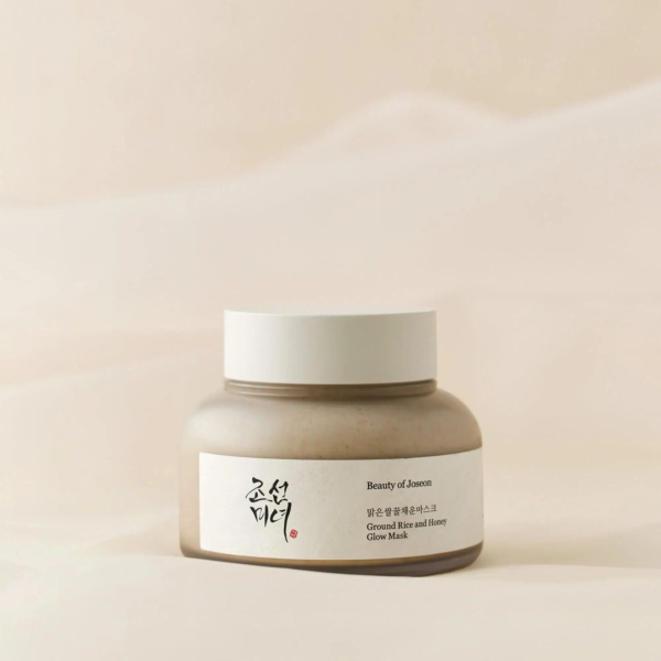 Un pot beige de soin « Beauty of Joseon » étiqueté « Masque Éclat Racine de Ginseng et Miel » se dresse sur un fond doux et neutre. Le pot présente un design simple et élégant, avec des caractères coréens sur l'étiquette. Dakar