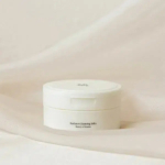 Un pot blanc étiqueté « Baume Nettoyant Éclat » sur un fond en tissu beige doux. Dakar