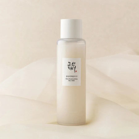 Une bouteille en verre dépoli avec un bouchon blanc, étiquetée « Glow-Repairing Face Milk » en caractères anglais et coréens, placée sur un fond en tissu doux de couleur crème. Dakar