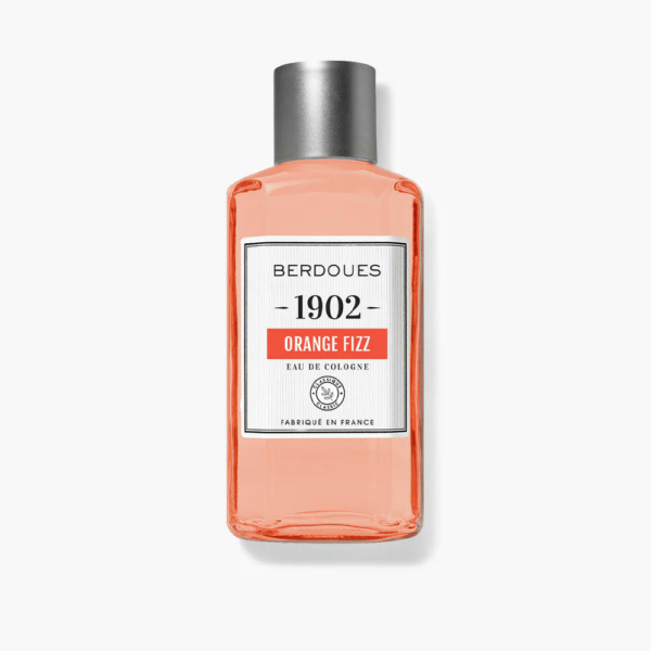 Une bouteille d'Eau de Cologne Berdoues 1902 Orange Fizz. Le flacon transparent contient un liquide orange et est muni d'un bouchon argenté. L'étiquette comporte le nom de la marque, le nom du produit et la mention « Fabriqué en France ». Dakar
