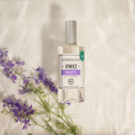 Un flacon d'eau de Cologne Berdoues 1902 Violette est posé sur une surface légère et texturée. Des fleurs violettes sont astucieusement disposées autour du flacon, complétant son esthétique. Dakar