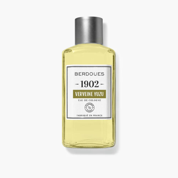 Une bouteille d'Eau de Cologne Berdoues 1902 Verveine Yuzu. Transparente, elle est munie d'un bouchon argenté et contient un liquide jaune. L'étiquette affiche la marque et le nom du produit en noir et vert sur fond blanc. Dakar