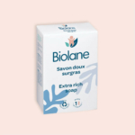Boîte de savon extra-riche Biolane sur fond beige. L'emballage est orné d'un texte bleu et vert et d'un logo représentant une silhouette humaine stylisée et des feuilles. L'étiquette indique qu'il est testé dermatologiquement, recyclable et fabriqué en France. Dakar