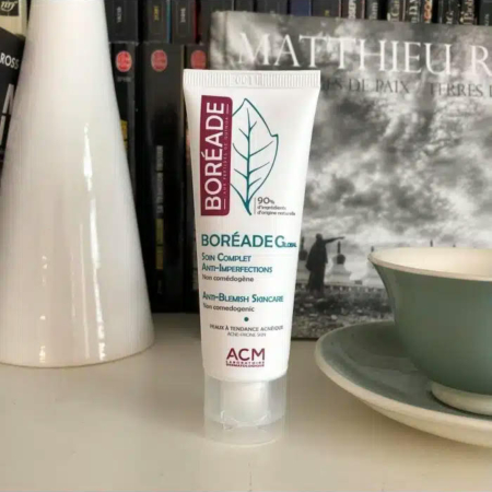 Un tube de soin anti-imperfections Boréade CL est posé sur une étagère, avec en arrière-plan flou des livres, un vase blanc et une tasse bleu sarcelle avec sa soucoupe. Le produit revendique des propriétés non comédogènes et anti-imperfections. Dakar