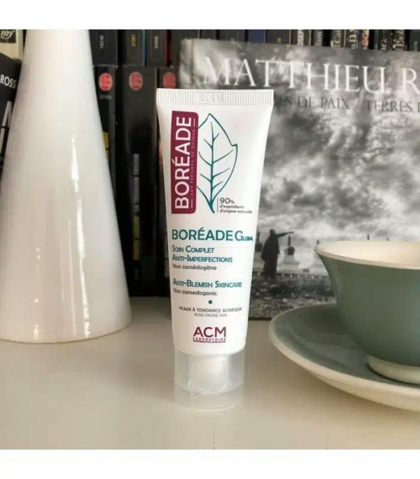 Un tube de soin anti-imperfections Boréade CL est posé sur une étagère, avec en arrière-plan flou des livres, un vase blanc et une tasse bleu sarcelle avec sa soucoupe. Le produit revendique des propriétés non comédogènes et anti-imperfections. Dakar
