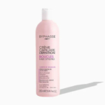 Un flacon rose de Crème Capillaire Définition Byphasse pour cheveux bouclés. Le texte sur le flacon souligne ses propriétés nourrissantes, volumatrices et anti-frisottis grâce à la provitamine B5 et à l'aloe vera. Le flacon est de 250 ml. Dakar