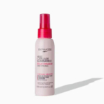 Un flacon vaporisateur d'Huile Capillaire Illuminatrice Byphasse, conçu pour les cheveux colorés. Blanc avec des touches de rose et de rouge, il est orné d'un texte en français et en anglais. Il est placé sur un fond clair et uni. Dakar