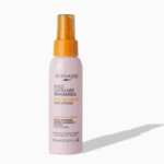 Un flacon d'huile capillaire réparatrice Byphasse avec vaporisateur. L'étiquette présente des touches orange et jaune, ainsi qu'un texte détaillant ses propriétés nourrissantes et anti-frisottis. Contient 100 ml. Les ombres créent un léger contraste sur le fond. Dakar