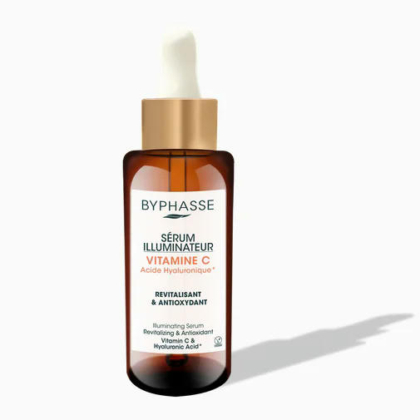 Un flacon en verre brun avec un bouchon compte-gouttes. L'étiquette indique « Byphasse Sérum Illuminateur Vitamine C Acide Hyaluronique, Revitalisant & Antioxydant ». Le flacon projette une ombre sur un fond clair. Dakar