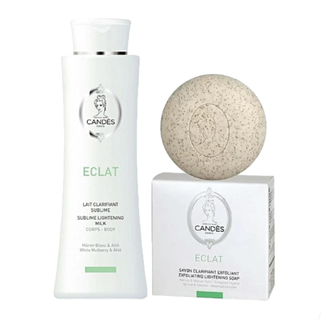 Un flacon et un emballage de lait éclaircissant Candès Éclat à la mûre blanche et aux AHA, à côté d'un savon exfoliant éclaircissant. Le flacon et l'emballage sont blancs avec des touches de vert. Le savon est moucheté et arrondi. Dakar