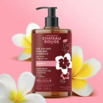 Un flacon de Gel Nettoyant Extra Riche Château Rouge aux fleurs de Monoï sur fond rose. Ce gel pour le visage et le corps, sans savon, contient 95 % d'ingrédients d'origine naturelle et est présenté dans un flacon de 750 ml. Dakar