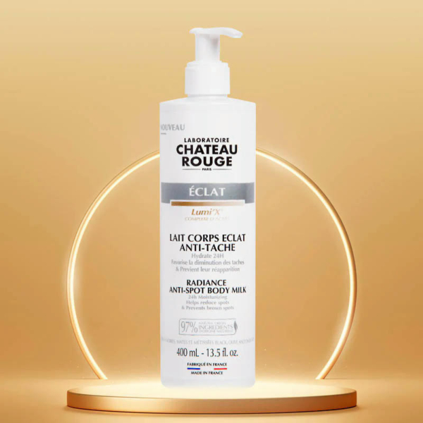Un flacon de Lait Corps Anti-Taches Éclat Château Rouge, muni d'une pompe, est placé sur un fond circulaire doré et lumineux. L'étiquette souligne sa conception pour réduire l'apparence des taches et sa composition à 97 % d'ingrédients d'origine naturelle. Dakar
