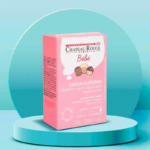 L'image montre une boîte rose de savon extra-riche Château Rouge Paris Bébé pour bébés et enfants, présentée sur une plateforme circulaire bleu sarcelle. La boîte présente des visages d'enfants dessinés et un texte détaillant les informations produit. Le fond est un dégradé bleu sarcelle. Dakar