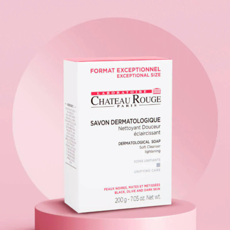 L'image montre une boîte rose et blanche de savon dermatologique Château Rouge Paris, format exceptionnel. Elle présente des informations sur ses propriétés éclaircissantes et unifiantes. Le fond est rose clair avec des motifs circulaires abstraits. Dakar