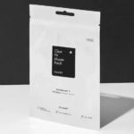 Un paquet blanc de patchs Clear Fit Master de COSRX. L'emballage est minimaliste, avec un carré noir portant le nom du produit. Il contient 18 patchs. Le fond est d'une teinte unie et neutre. Dakar