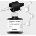 Gros plan sur un flacon de sérum COSRX Hyaluronic Acid 3 avec un compte-gouttes déversant une goutte. L'étiquette indique « Acides aminés + NP de céramide » pour l'hydratation et la rétention d'eau. Une structure moléculaire est illustrée en arrière-plan. Dakar