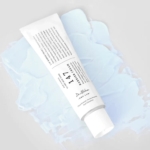 Un tube blanc étiqueté « Dr Althea 147 Crème Barrière au Resvératrol et à l'Adénosine 50 ml » est posé en diagonale sur un fond texturé bleu clair, avec un texte et une marque élégants mis en valeur par son bouchon blanc immaculé. Dakar