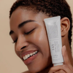 Une personne souriante, les yeux fermés, tient un tube de crème 345 Relief près de son visage. Aux cheveux courts et bouclés, elle applique la crème, révélant une peau lisse et éclatante. Dakar
