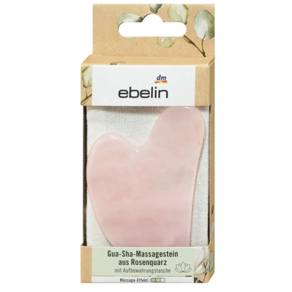 Emballage d'une pierre de massage Gua Sha en quartz rose Ebelin, ornée d'un motif floral. La pierre rose en forme de cœur est présentée dans une fenêtre transparente. Le texte en allemand décrit l'article comme un outil de massage avec pochette de rangement. Dakar