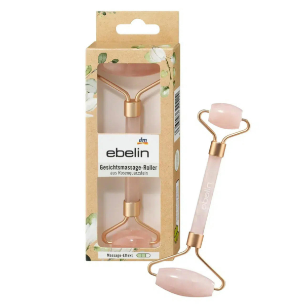 Un rouleau facial en quartz rose aux accents dorés est présenté à côté de son emballage floral. La boîte est dotée d'une fenêtre affichant le rouleau et porte la marque « ebelin » avec un texte supplémentaire en allemand. Dakar