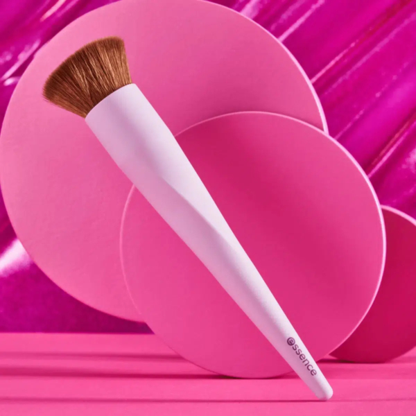 Un pinceau de maquillage avec un manche rose et des poils marron est présenté sur un fond vibrant de cercles roses superposés et d'une surface magenta brillante. Dakar