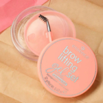 Coffret gel rehausseur de sourcils Essence couleur pêche, composé d'un flacon transparent et d'un petit pinceau spoolie sur une surface texturée beige. Le couvercle affiche les informations produit en blanc et argent. Dakar