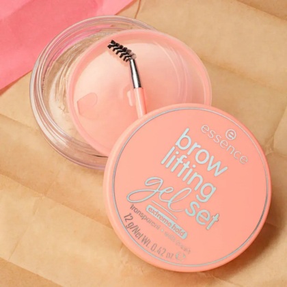 Coffret gel rehausseur de sourcils Essence couleur pêche, composé d'un flacon transparent et d'un petit pinceau spoolie sur une surface texturée beige. Le couvercle affiche les informations produit en blanc et argent. Dakar